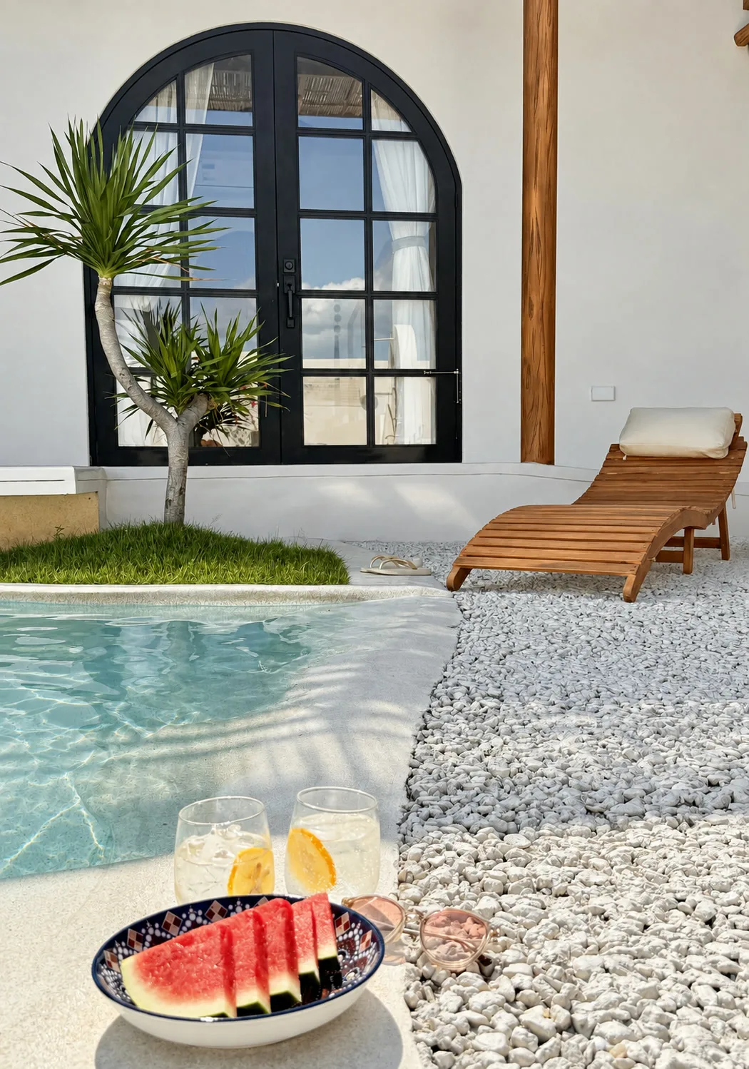 Poolside refreshments beside white pebbles, a compact lawn pocket, and a tropical accent plant