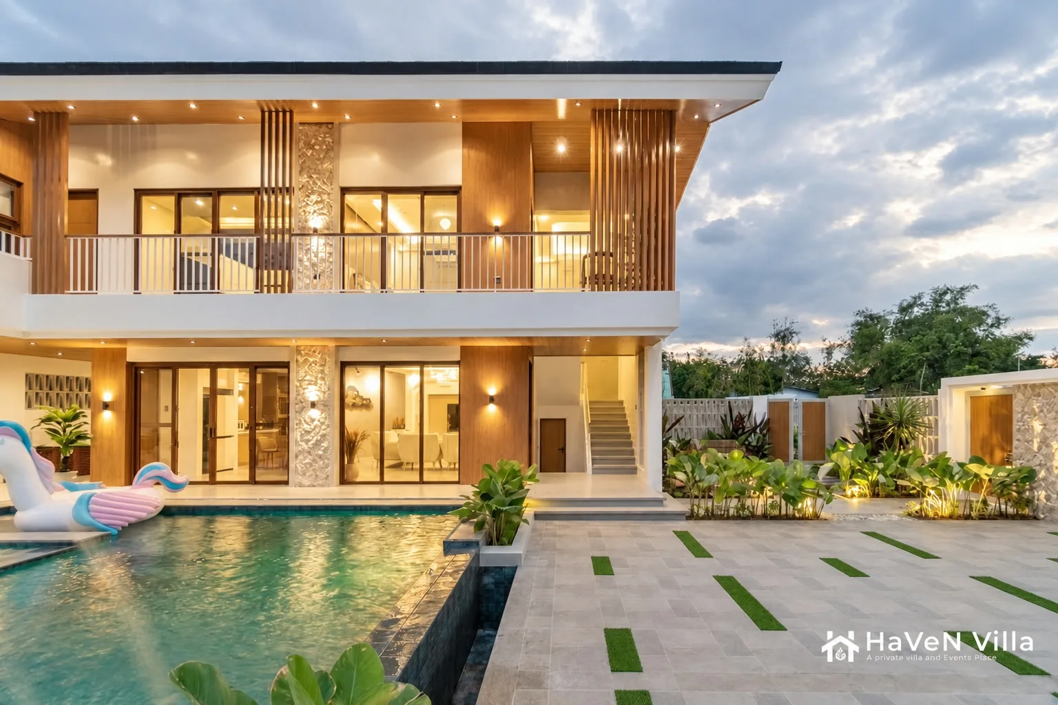 Evening pool view with warm interior lights, timber screens, and tropical border planting