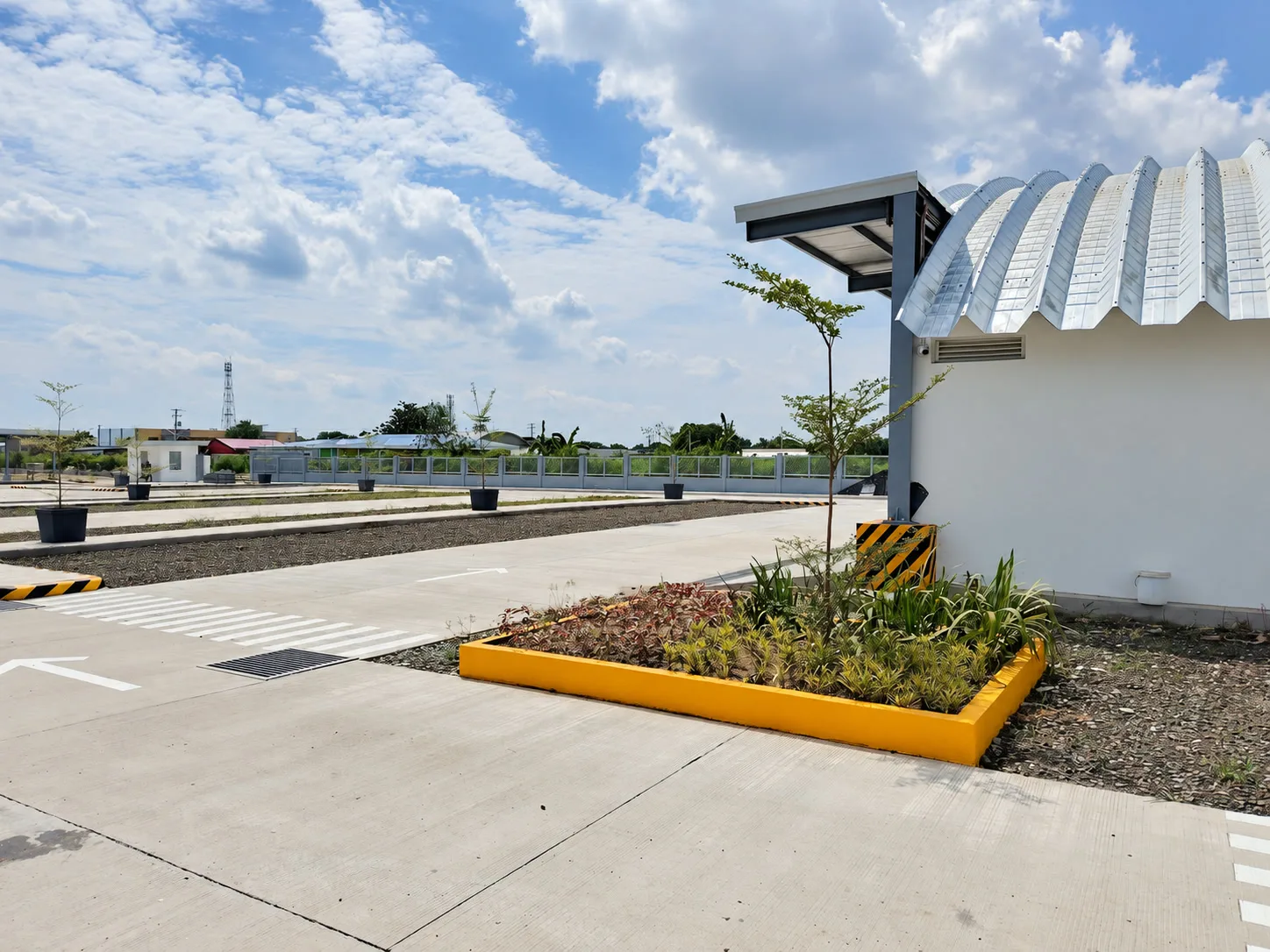 Concrete service lanes and curved-roof building around a planted island with young trees