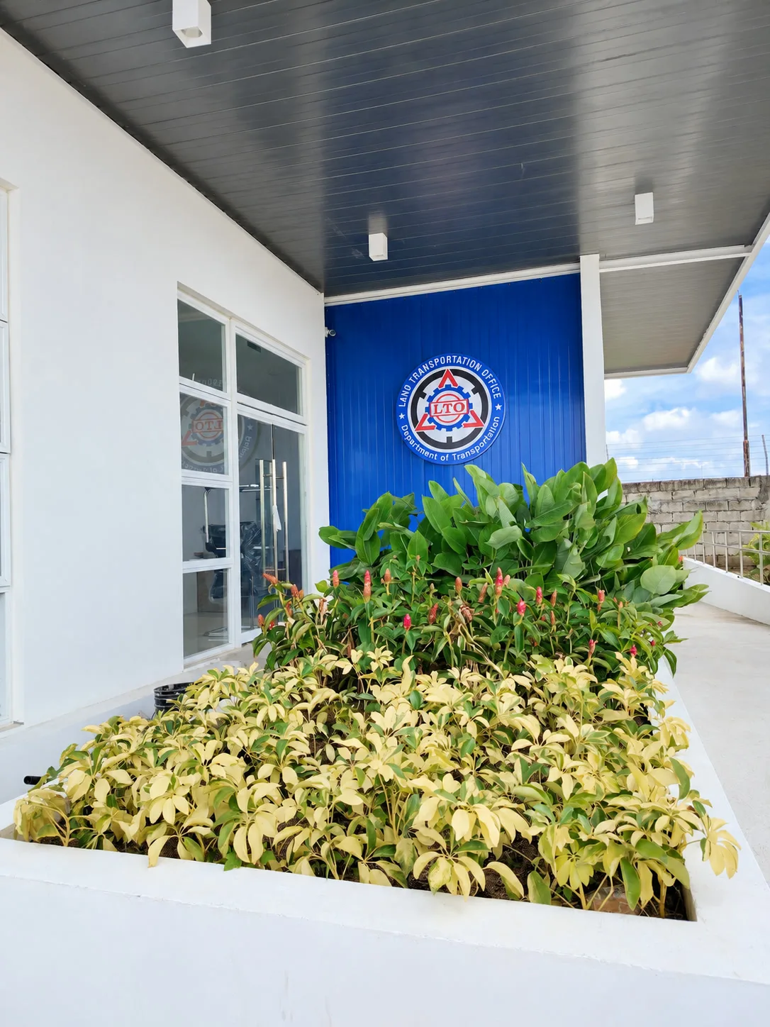 Raised entry planter with layered foliage and flowers below the LTO emblem
