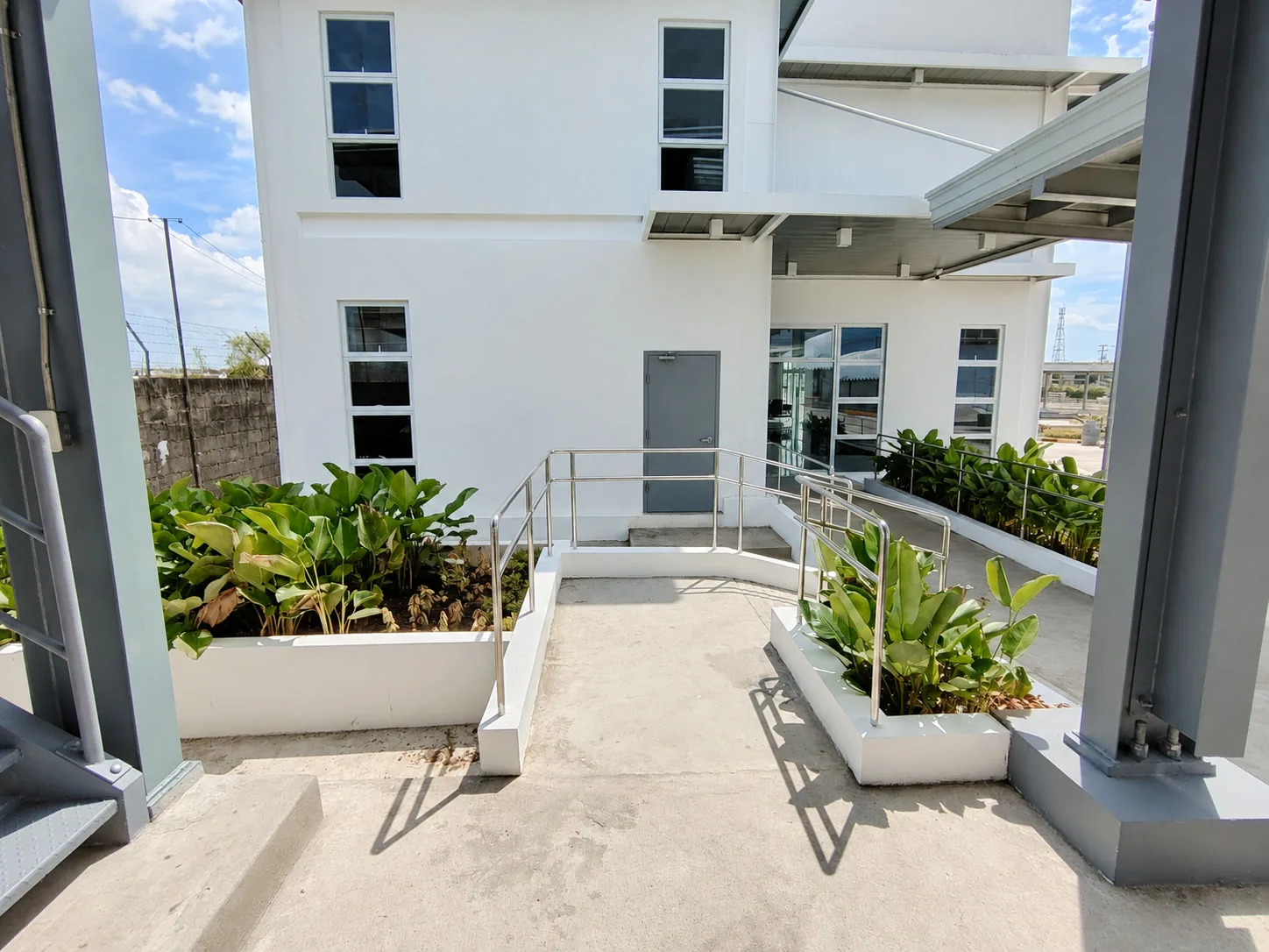 Accessible concrete courtyard with ramp rails, canopies, and raised planted beds