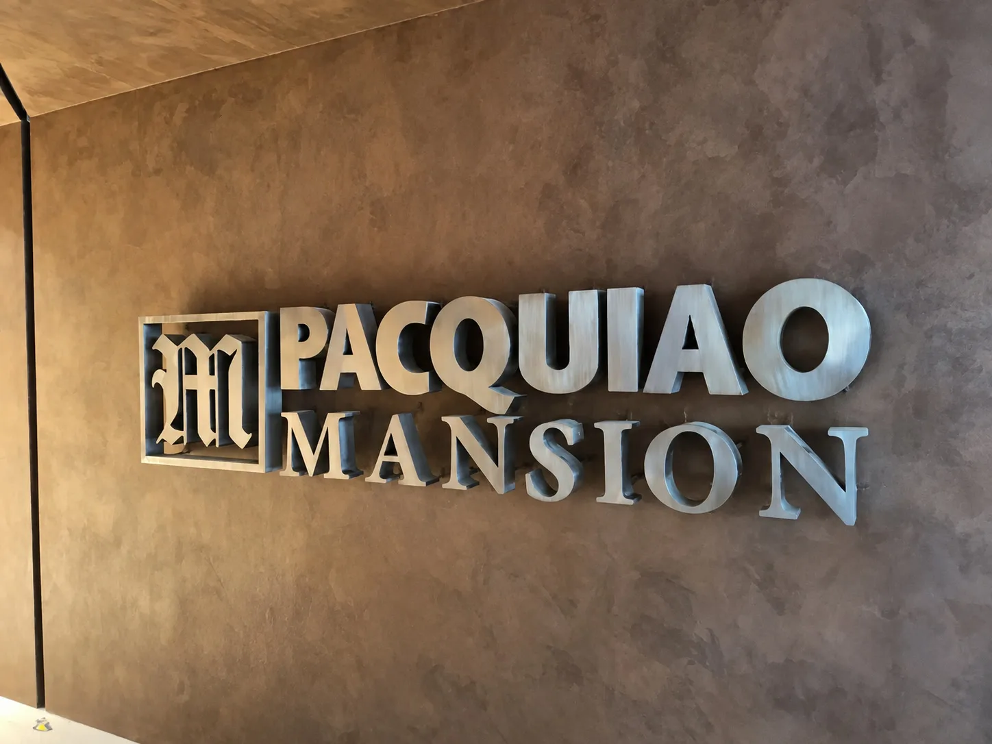 Brushed-metal Pacquiao Mansion sign mounted on a warm textured wall